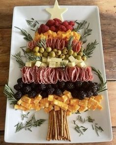 a christmas tree made out of fruits and cheeses on a white platter with olives