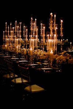 a long table with candles and flowers on it in front of a black background at an event