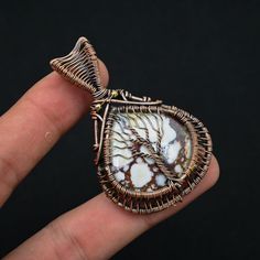 a hand holding a wire wrapped pendant with a tree on it