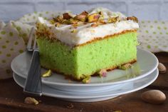 a piece of green cake with white frosting and pistachios on top