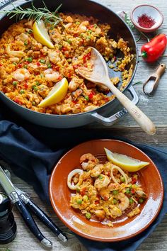 a pan filled with shrimp and rice on top of a wooden table next to other dishes