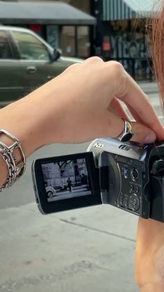 a woman is holding up a camera to take a picture on the side of the street