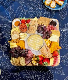 a platter filled with cheese, crackers and fruit on a blue table cloth