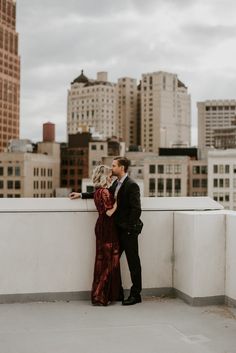 a man and woman standing next to each other on top of a roof in front of tall buildings