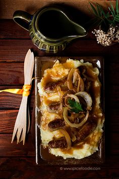 mashed potatoes with onions and gravy on a plate next to a serving spoon