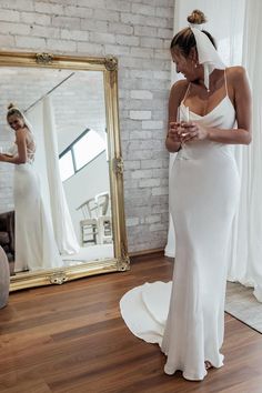 a woman standing in front of a mirror wearing a wedding dress