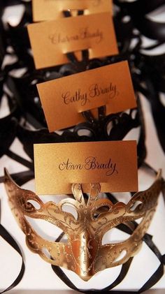 masks with name cards attached to them sitting on black ribboned place card holder holders