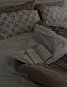 an open book laying on top of a bed next to pillows and blankets in a bedroom