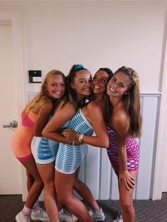 four girls are posing for the camera in their bathing suits and shorts, one girl is holding her arm around another woman's shoulder