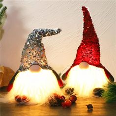 two red and silver gnome hats sitting on top of a wooden table next to pine cones