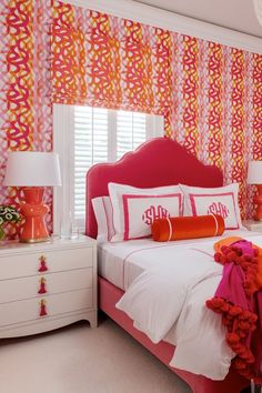 a bedroom decorated in pink and orange with white bedding, red headboard and pillows