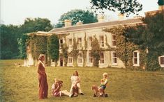 a group of children sitting on the grass in front of a large house with ivy covered walls