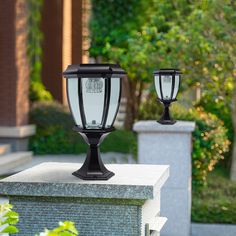 two black street lights sitting on top of a cement block in front of trees and bushes