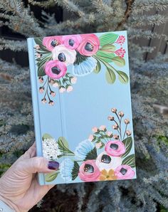 a hand holding up a notebook with flowers on it