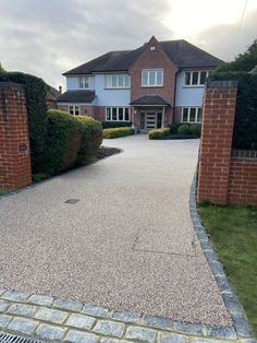 a driveway is shown with brick walls and grass around it, leading to a large house