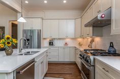 a white kitchen with sunflowers in the vase on the stove top and refrigerator