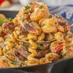 a spoon full of pasta with shrimp and other food items in it on a plate