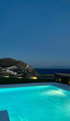 an empty swimming pool at night with the ocean in the backgroung and mountains in the background