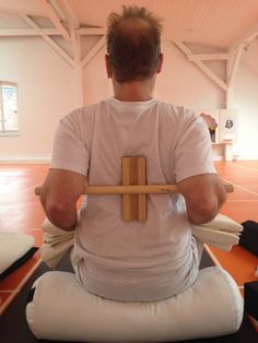 a man sitting on the floor with a wooden stick in his lap and wearing a white t - shirt