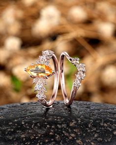 two wedding rings with an orange topazte surrounded by white diamonds on a rock