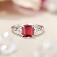 a close up view of a ring with a red stone and two white diamonds on it