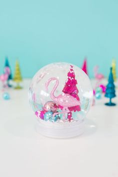 a pink flamingo in a snow globe surrounded by christmas trees and other holiday decorations