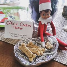 an elf is sitting in front of some cookies on a plate with a sign that says official cookie tester