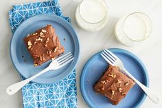 two blue plates topped with brownies next to glasses of milk and napkins on a white table