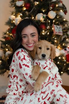 a woman holding a puppy in front of a christmas tree