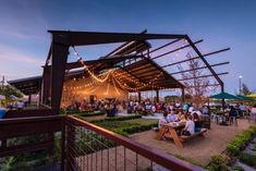 a group of people sitting at picnic tables under an awning with lights strung over them