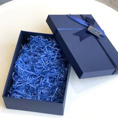 an open box with blue shredded paper in it on a white table next to a cup and saucer