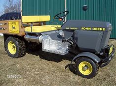 an old yellow and black tractor is parked in front of a green building with a sign that says john deere on it