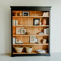 a bookshelf with baskets and pictures on the top shelf, next to other items