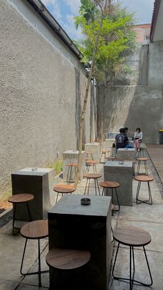 several tables and stools are lined up on the sidewalk near a wall with a tree