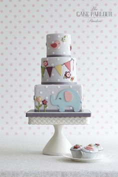 a three tiered cake with an elephant on top and cupcakes below it