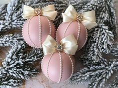 three pink ornaments with bows and pearls on them