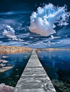 a long wooden dock extending into the ocean under a cloudy blue sky with white clouds