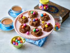 a plate with cookies and candy on it next to two cups of hot chocolates