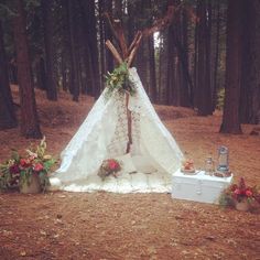 a teepee is set up in the woods with flowers and decorations around it,