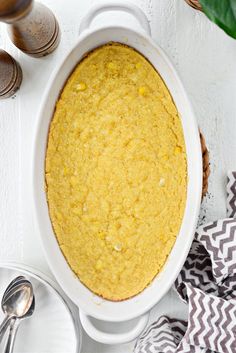 a casserole dish on a white table with spoons and napkins next to it