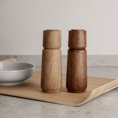 two wooden salt and pepper shakers sitting on a cutting board next to a bowl