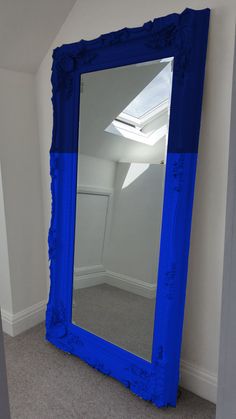 a large blue mirror sitting on top of a floor next to a white wall in a room