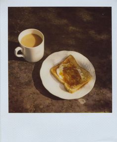 a cup of coffee and some food on a white plate next to a small piece of bread