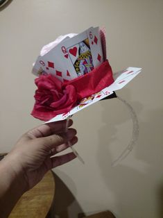 a person holding up a paper hat with playing cards on it and a red flower