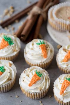 carrot cupcakes with white frosting and cinnamon sticks in the background on a table