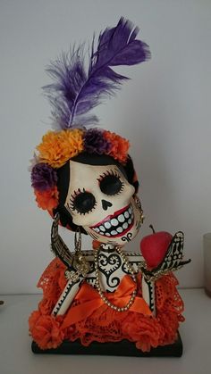 a skeleton figurine with an orange dress and purple feathers on it's head