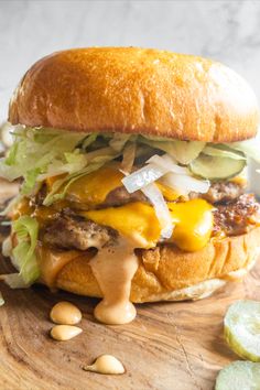 a cheeseburger on a wooden cutting board with pickles