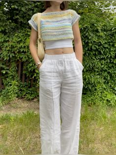 a woman wearing white pants and a cropped top standing in front of some bushes