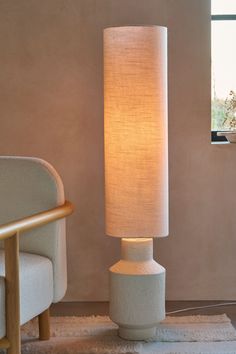 a white table lamp sitting on top of a rug next to a chair and window