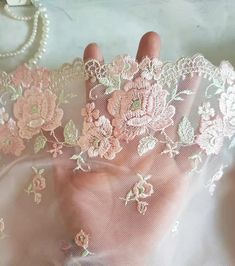 a hand that is covered in lace and flowers on top of a white cloth with pearls